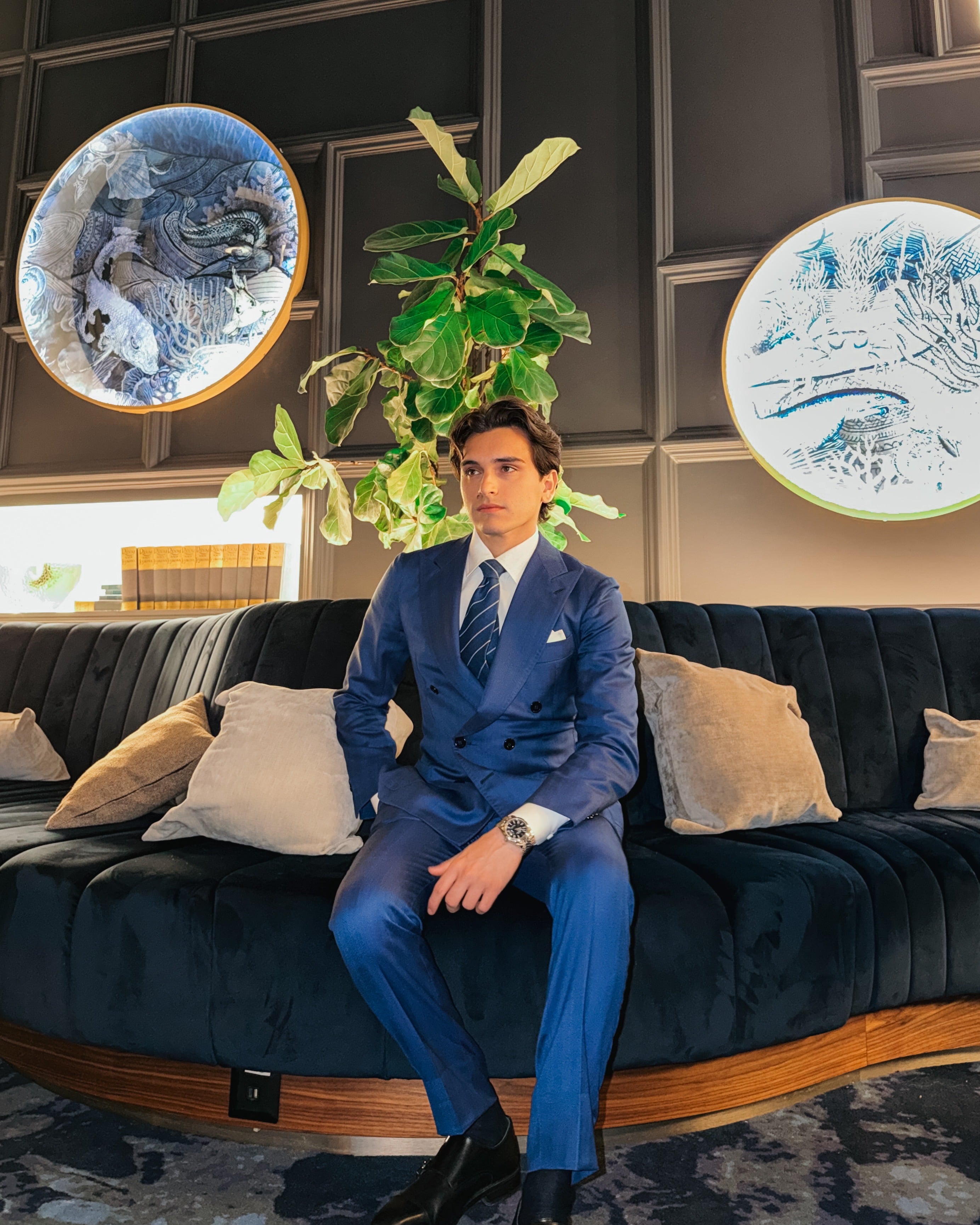 Aristide Tofani, third-generation Neapolitan tailor and influencer, seated in a royal-blue double-breasted suit in a contemporary luxury lounge.