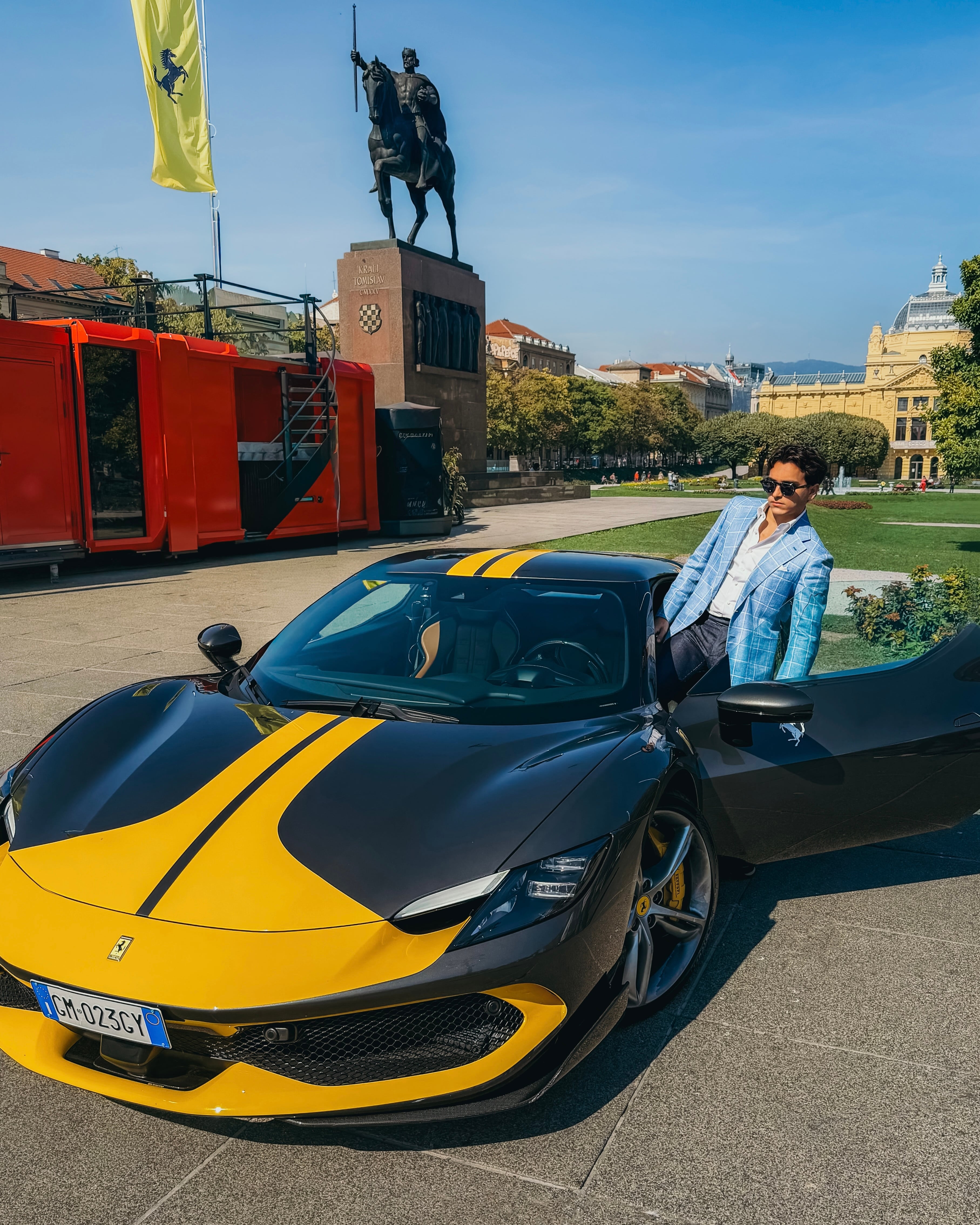 Aristide in a light windowpane blazer stepping from a sports car in a European square.