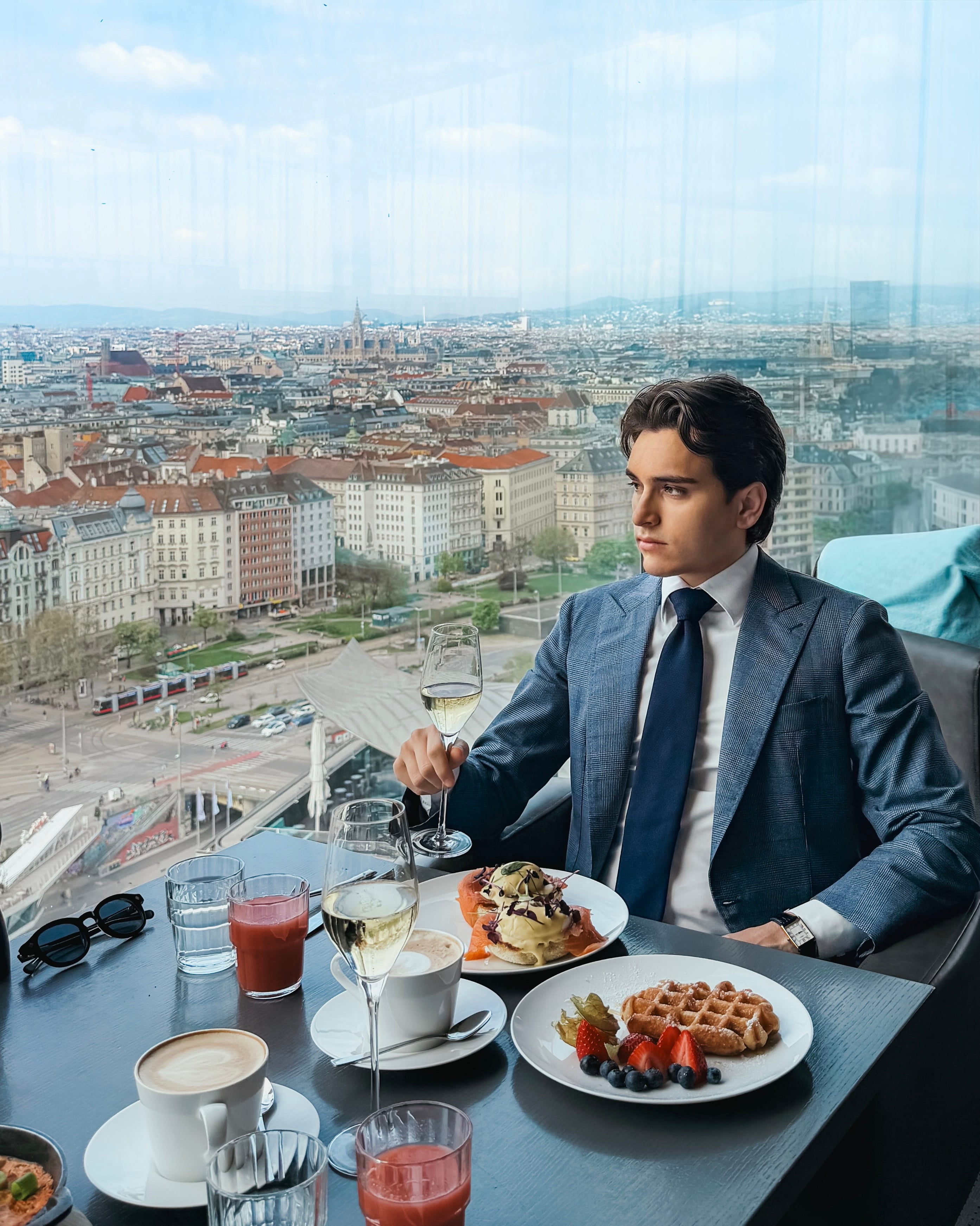 Aristide Tofani, third-generation Neapolitan tailor and influencer, in a blue-grey suit at a luxury brunch with a city view